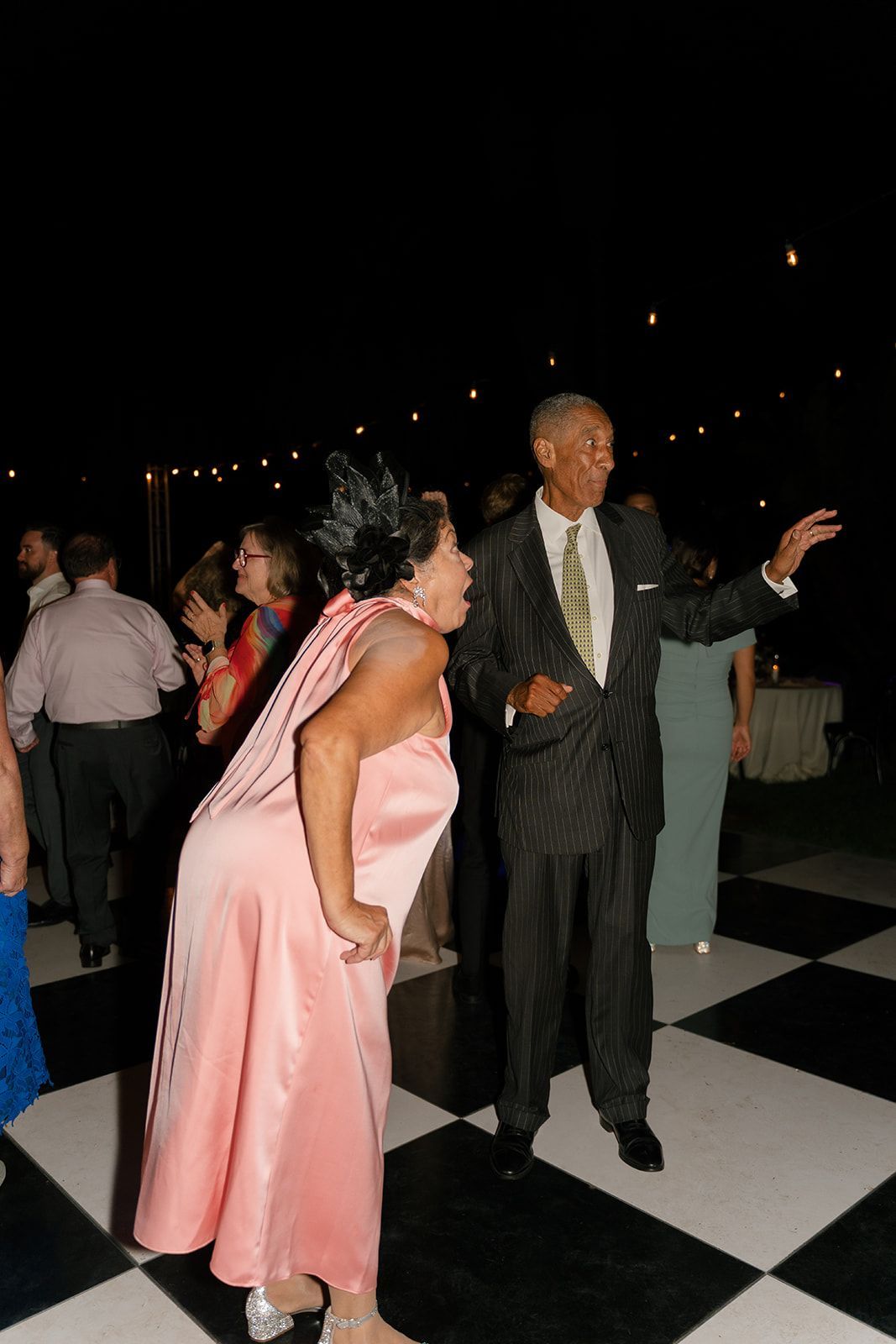 Two people dancing on a black-and-white checkered floor at a nighttime event