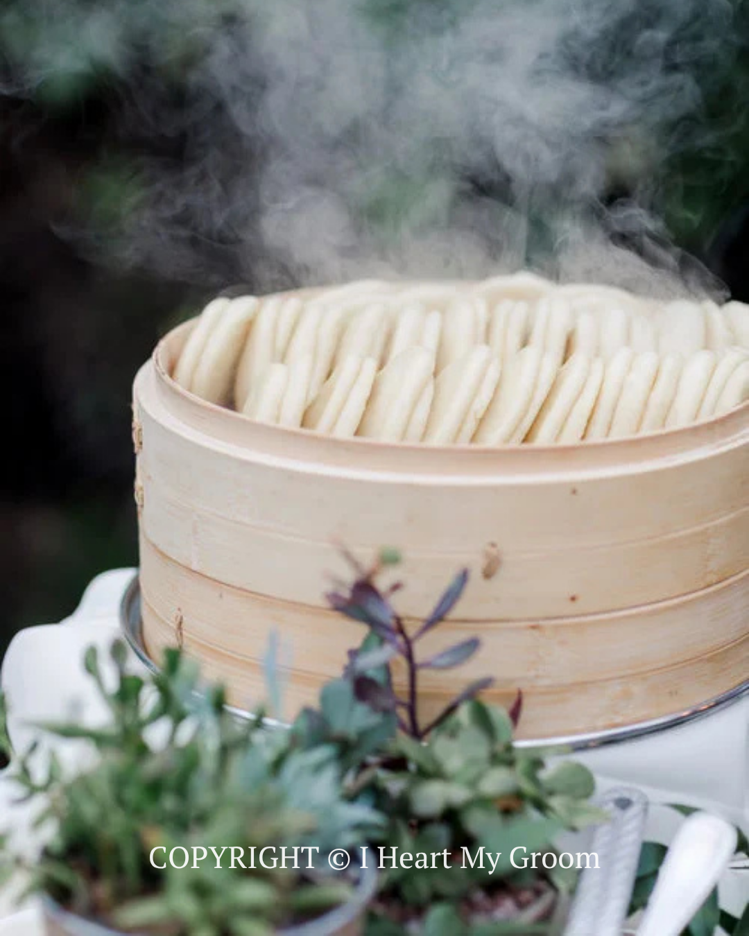 Steam rising from a bamboo steamer filled with dumplings, with blurred greenery in the foreground.