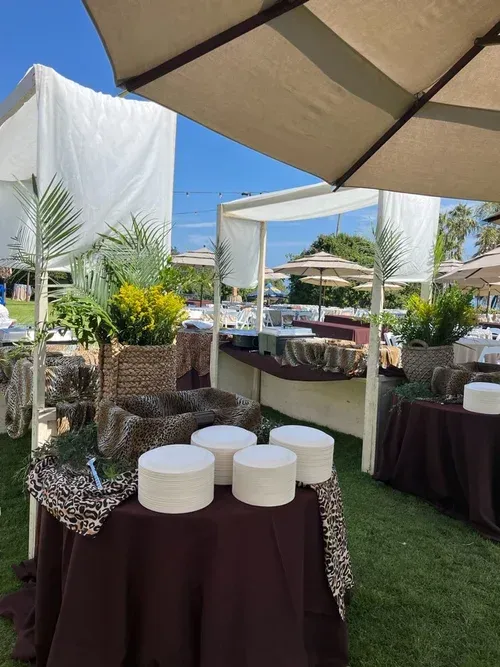 Outdoor buffet table with white-covered dishes under a beige canopy in a garden setting
