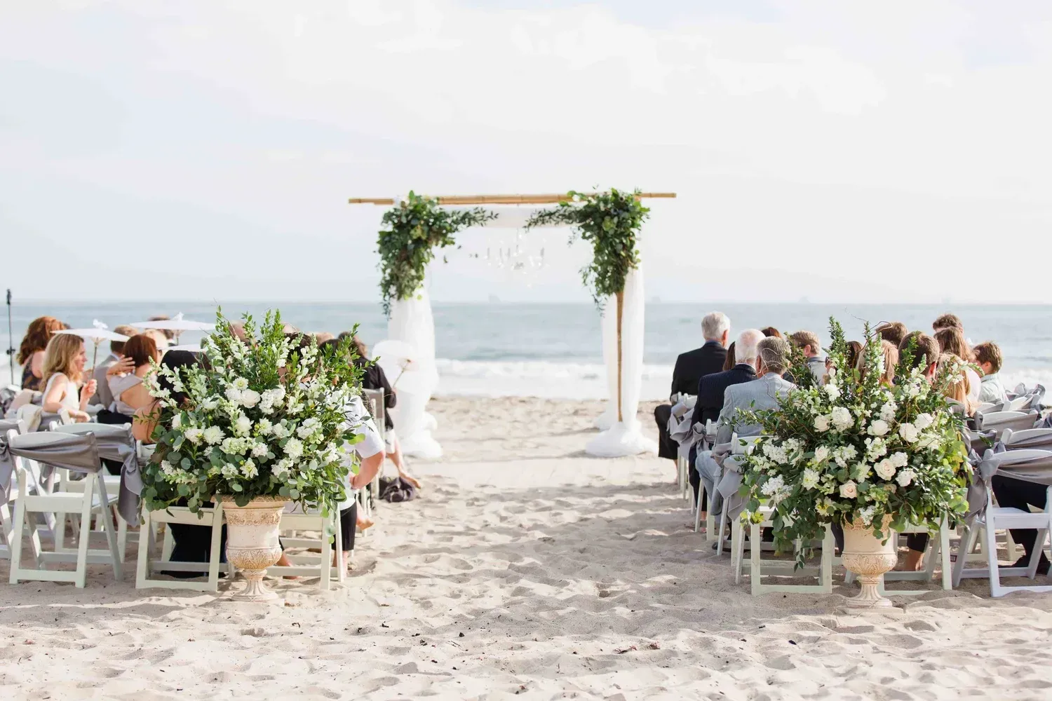 Beach wedding ceremony with floral arch, seated guests, and ocean backdrop