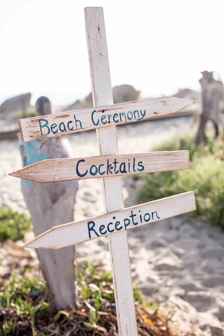 Rustic wooden arrow sign pointing to beach ceremony, cocktails, and reception at an outdoor wedding venue