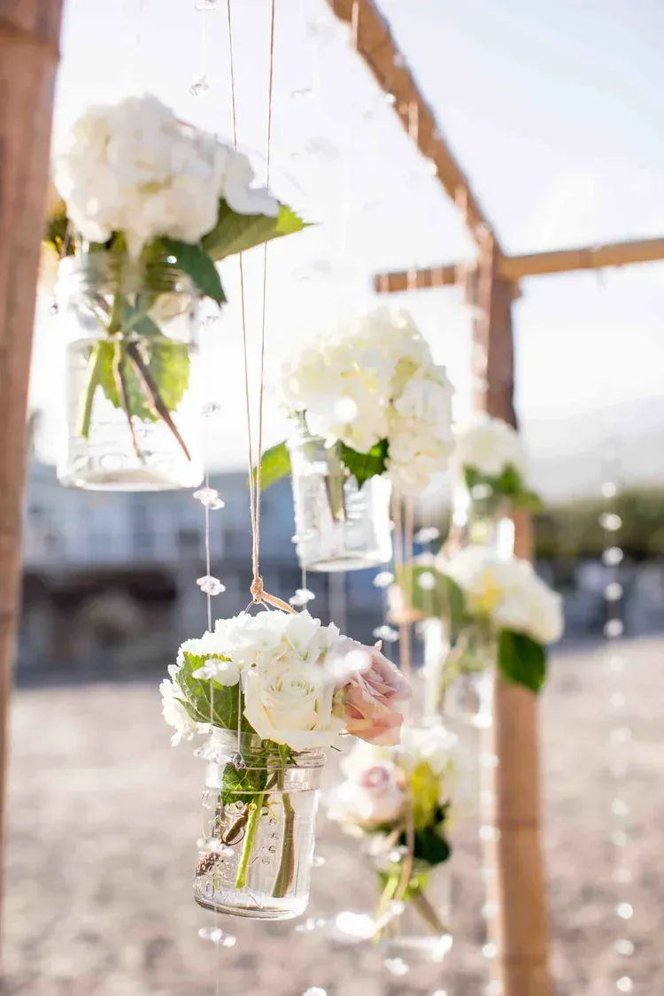 White flowers in hanging glass jars at an outdoor wedding or event setting.