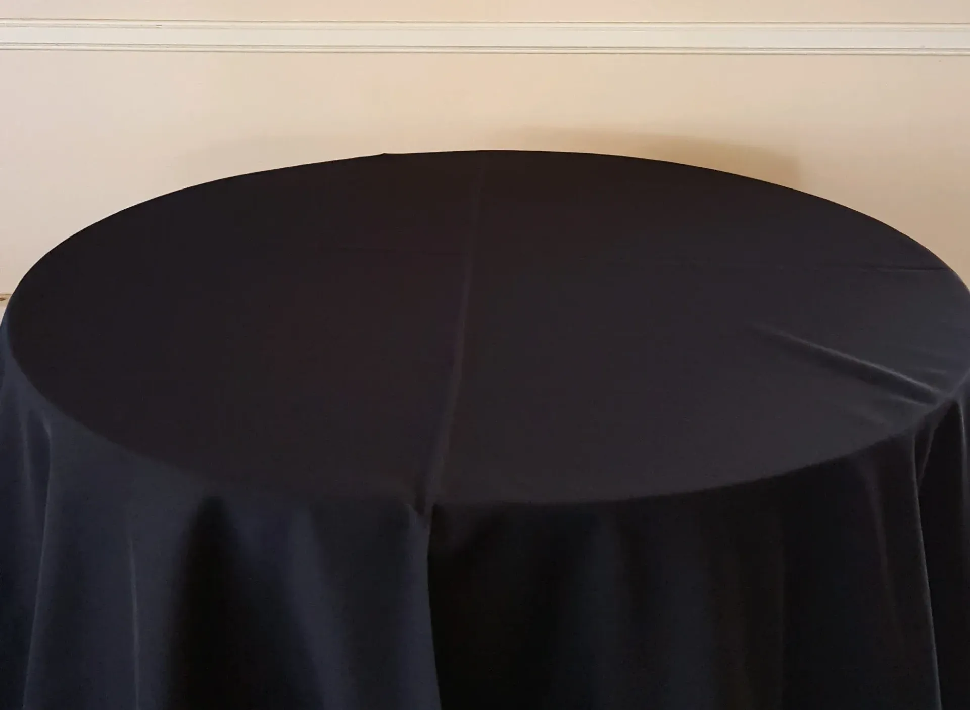 Round black table covered with a black tablecloth against a beige wall