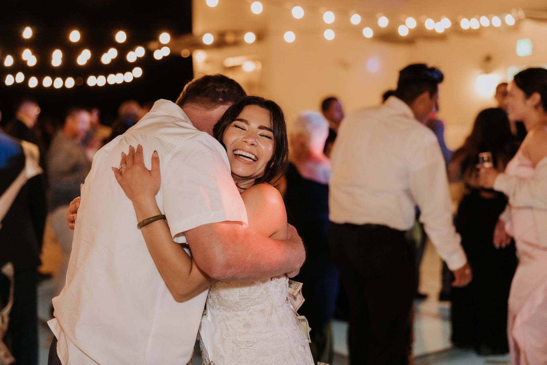 Couple embracing and smiling at a softly lit indoor party with string lights