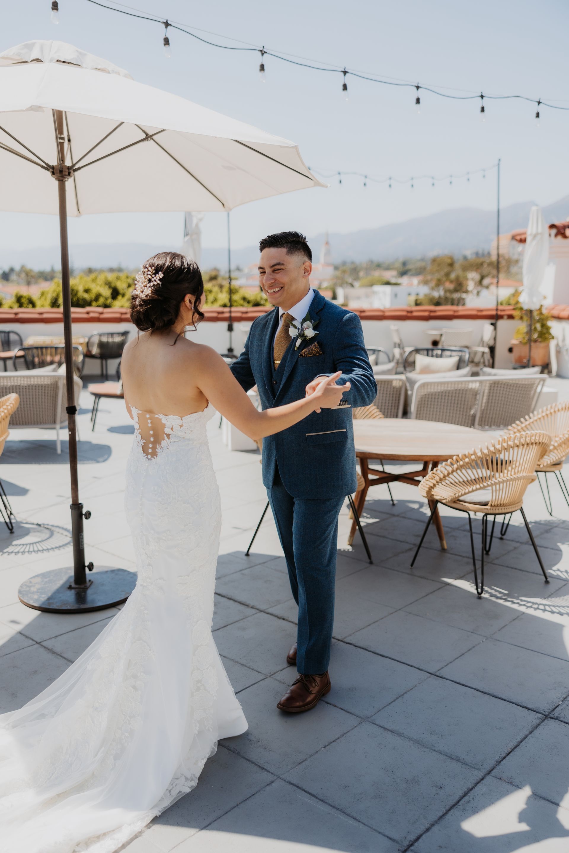 Bride and groom dancing on a rooftop terrace under string lights, holding hands and smiling