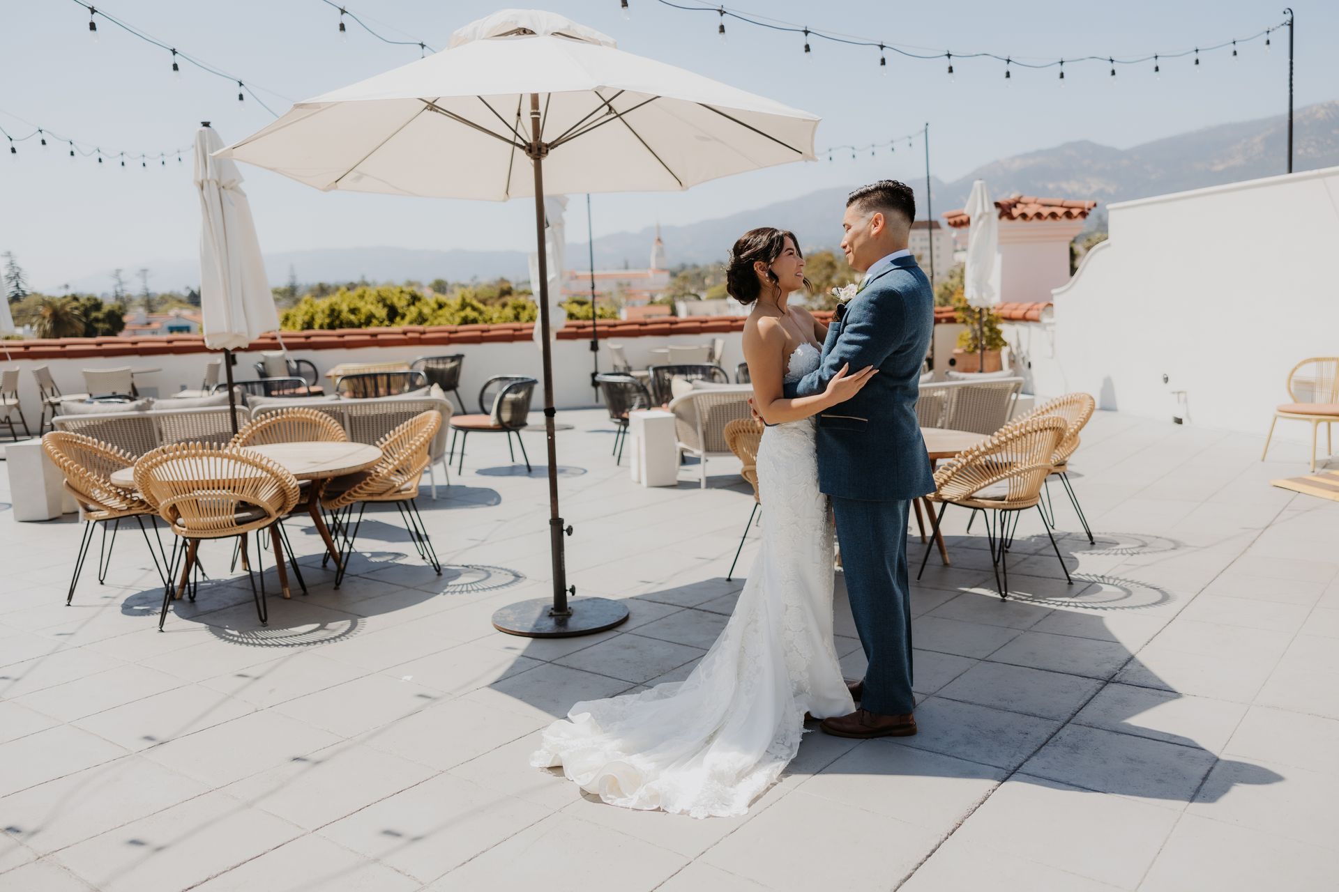 Couple embracing on a sunny rooftop patio with tables, umbrellas, and city skyline beyond
