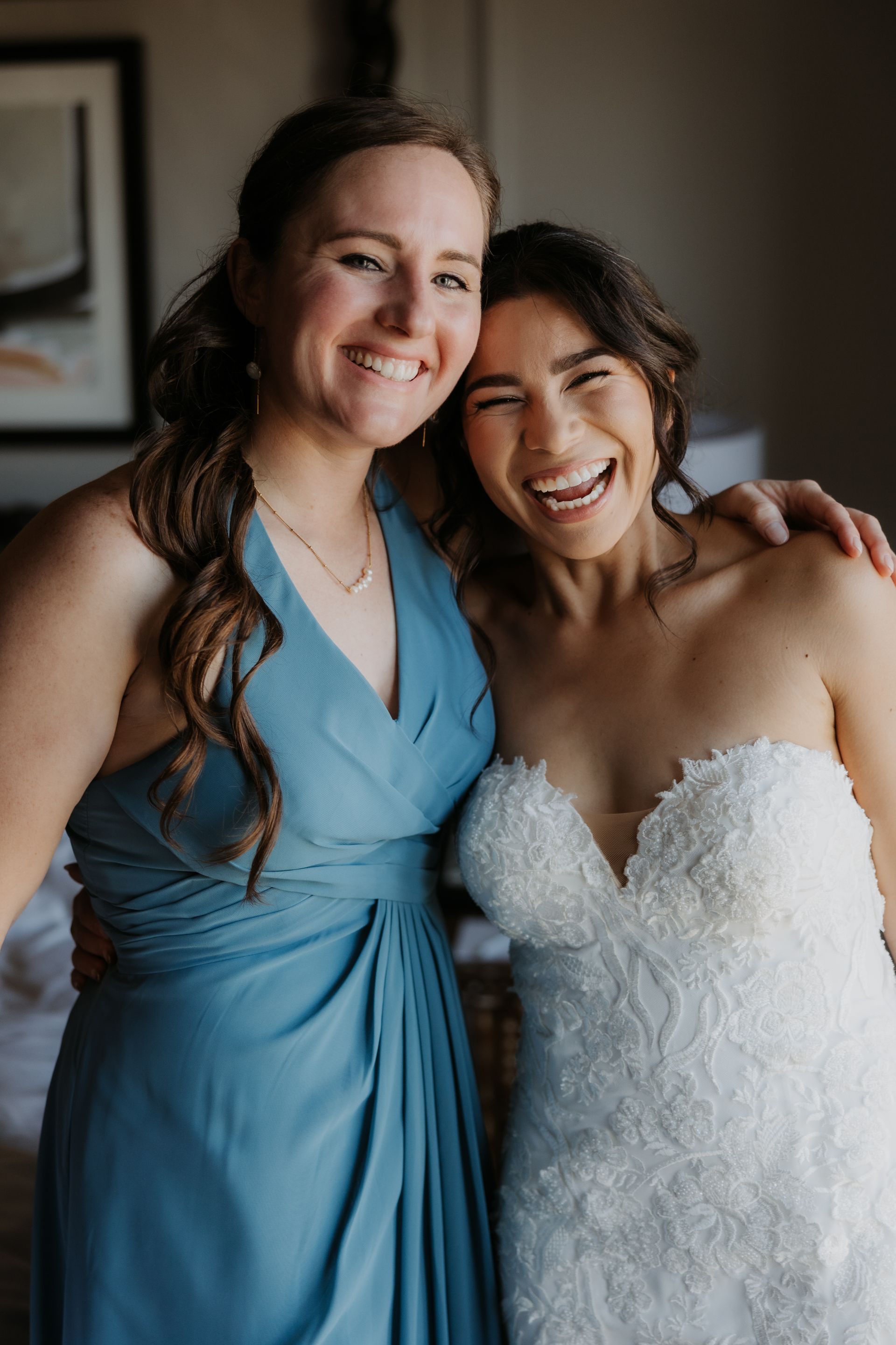 Two smiling people in blue and white dresses embrace indoors, likely at a wedding.