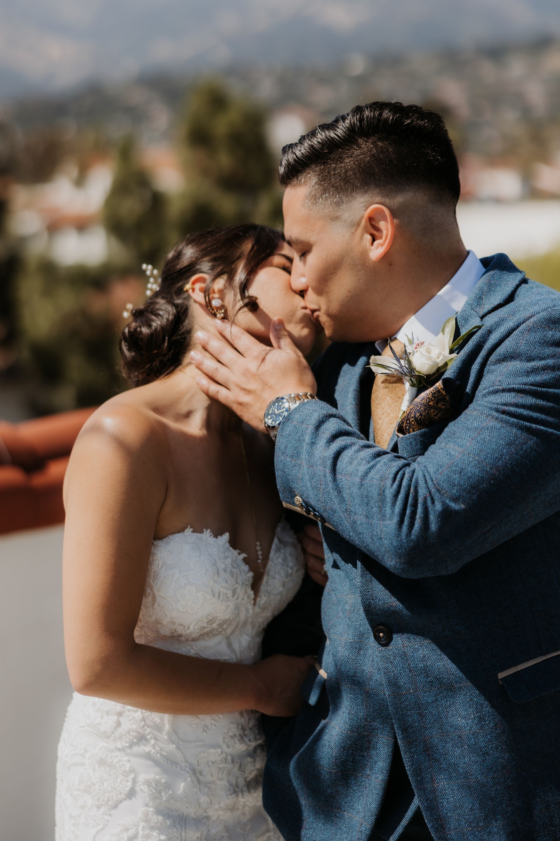 Bride and groom kissing outdoors, with mountains blurred in the background.