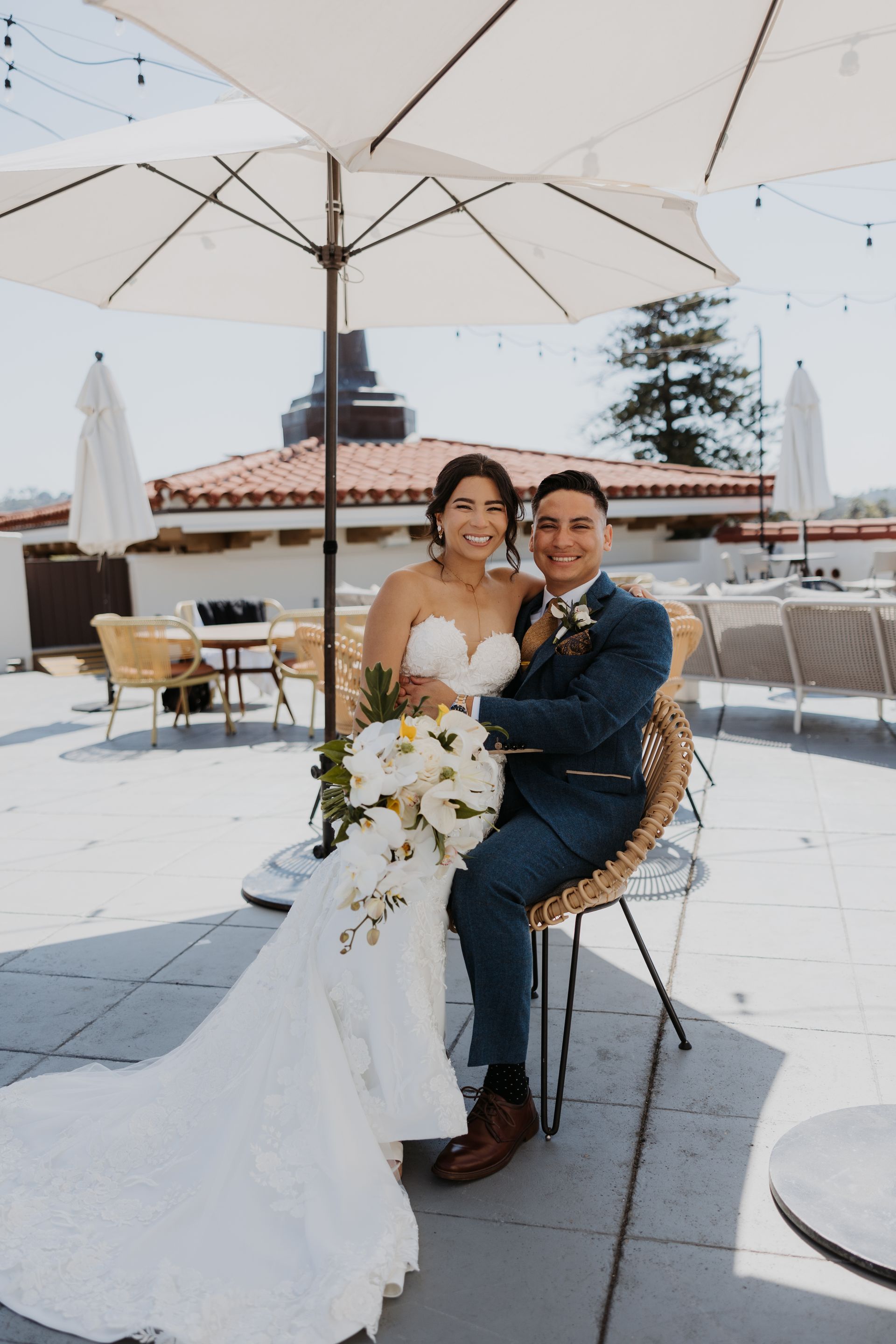 Bride and groom seated under a white umbrella on a snowy rooftop, smiling at the camera.