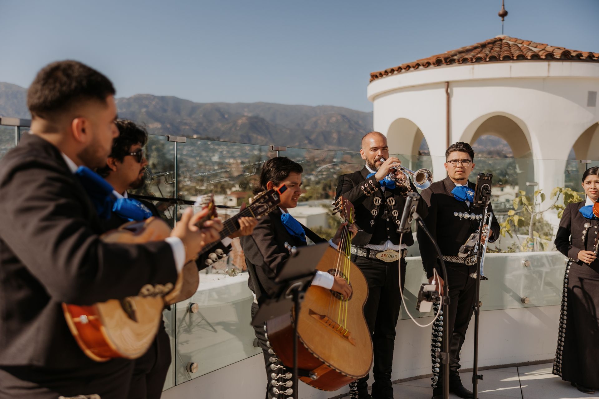 Mariachi band performing outdoors on a rooftop terrace with mountains in the background