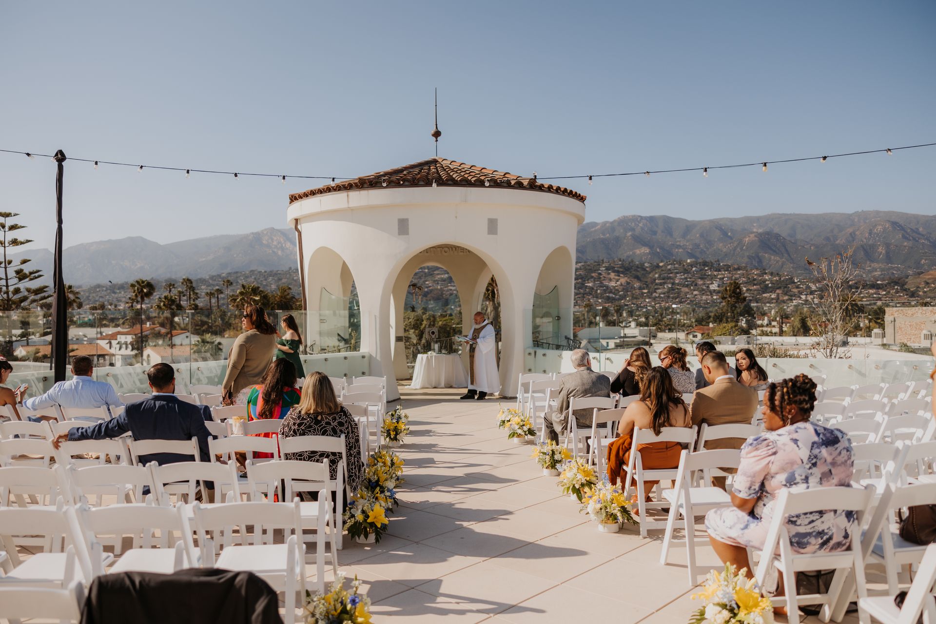 Outdoor wedding ceremony with white chairs, floral aisle, and a gazebo overlooking mountains