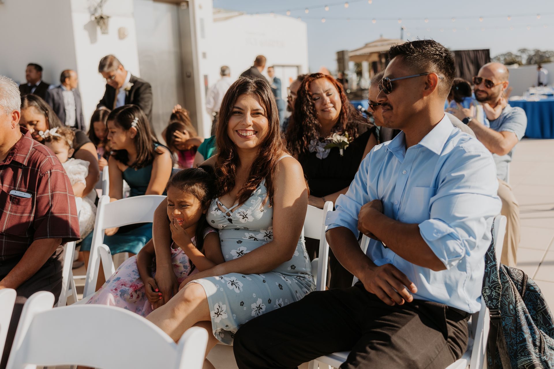 Two people seated outdoors at an event, smiling and talking among other guests.
