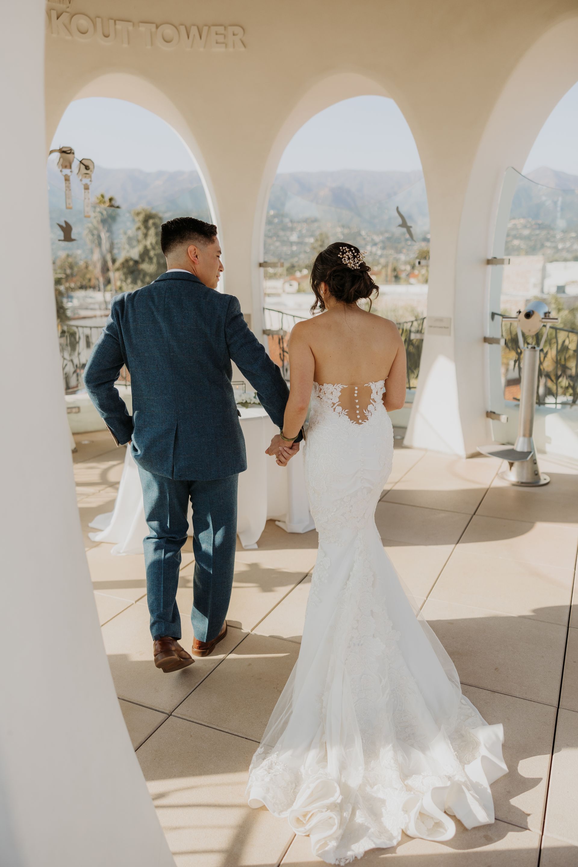 Bride and groom walking through white arches overlooking a city skyline