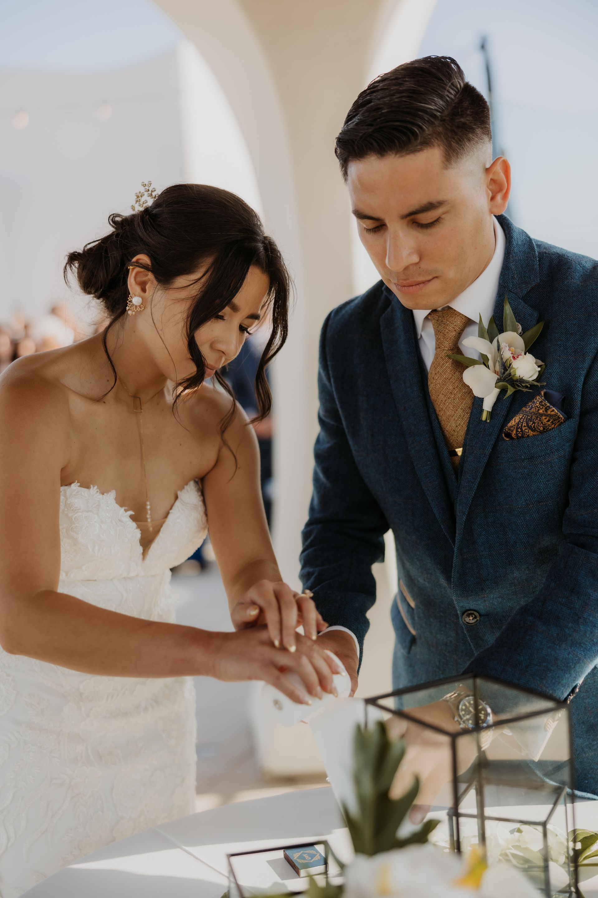 Bride and groom signing a document beside a lantern and small plant at a wedding ceremony