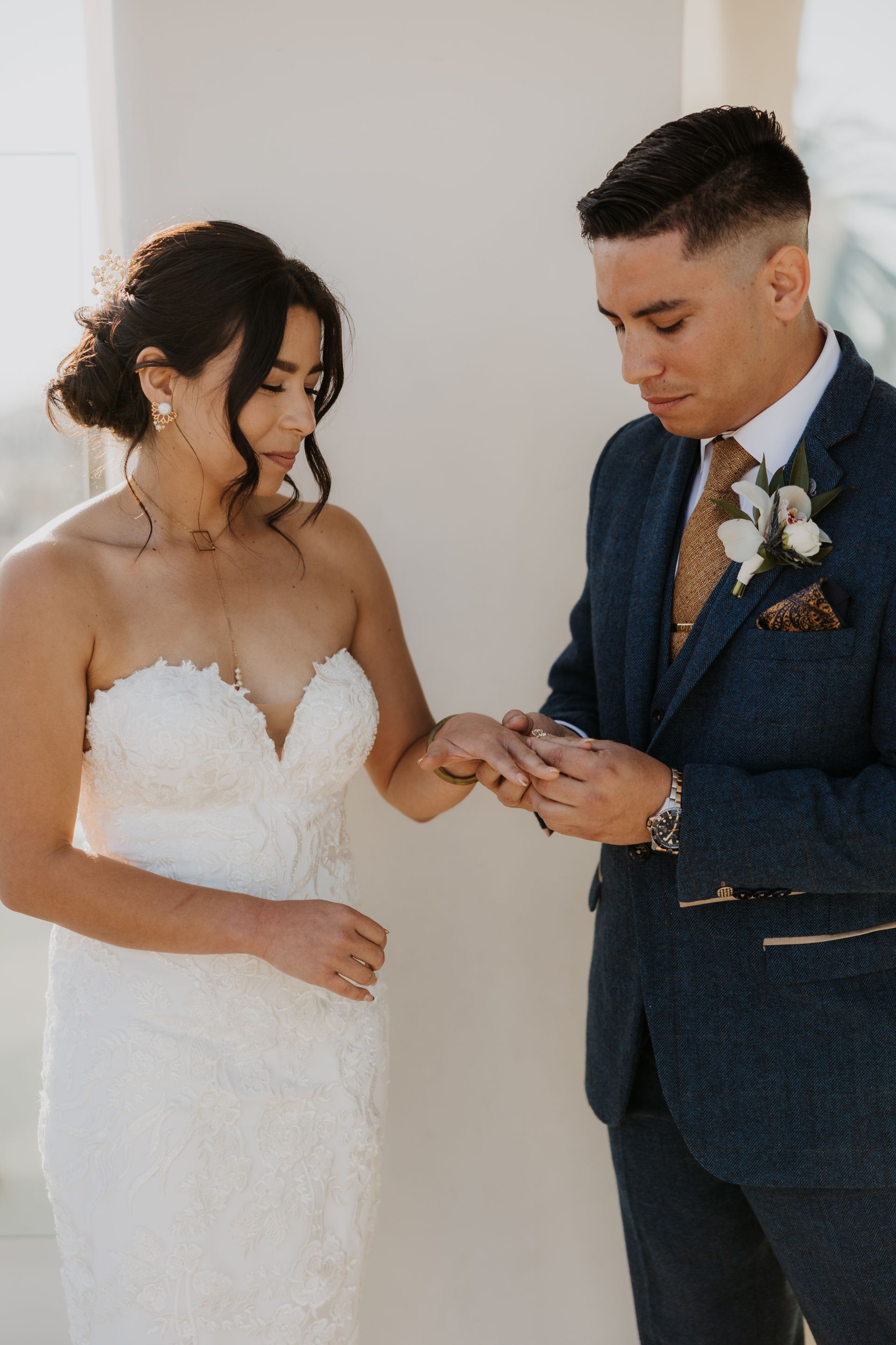 Bride in white gown and groom in navy suit exchanging rings at a wedding ceremony.