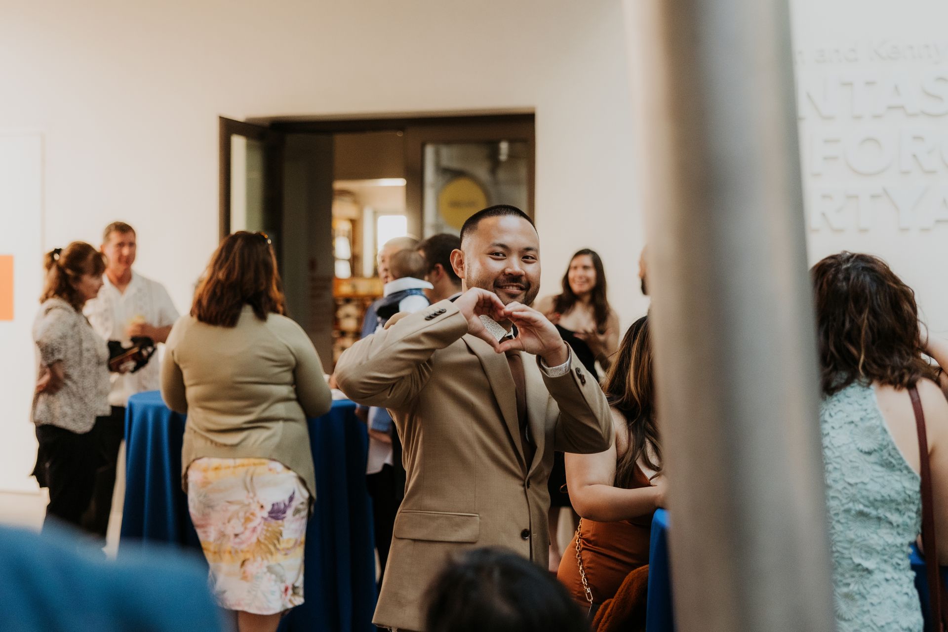 Man taking a selfie at a social gathering with people mingling in the background