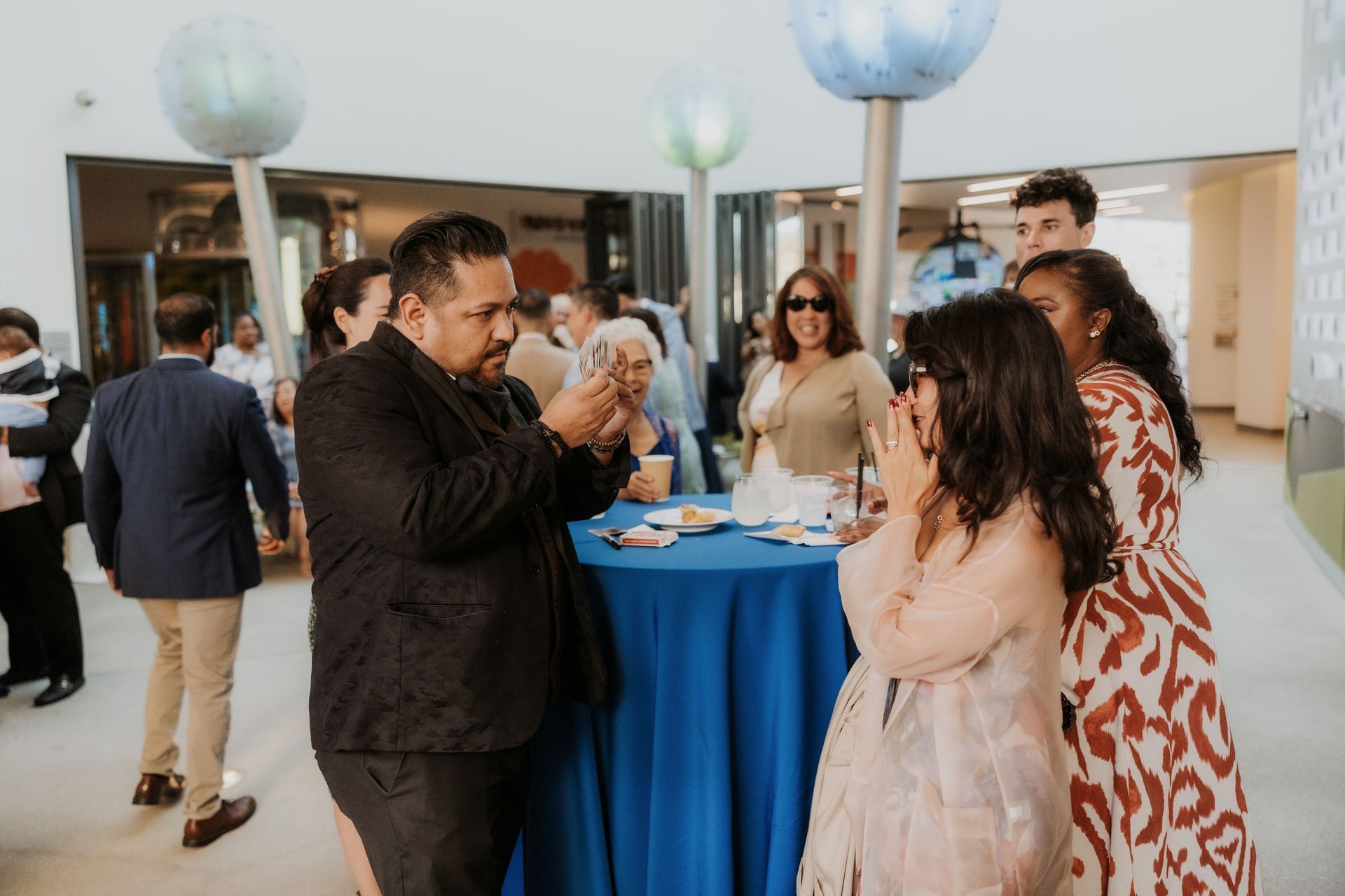 Guests mingling at a formal indoor reception around a blue table with drinks and snacks