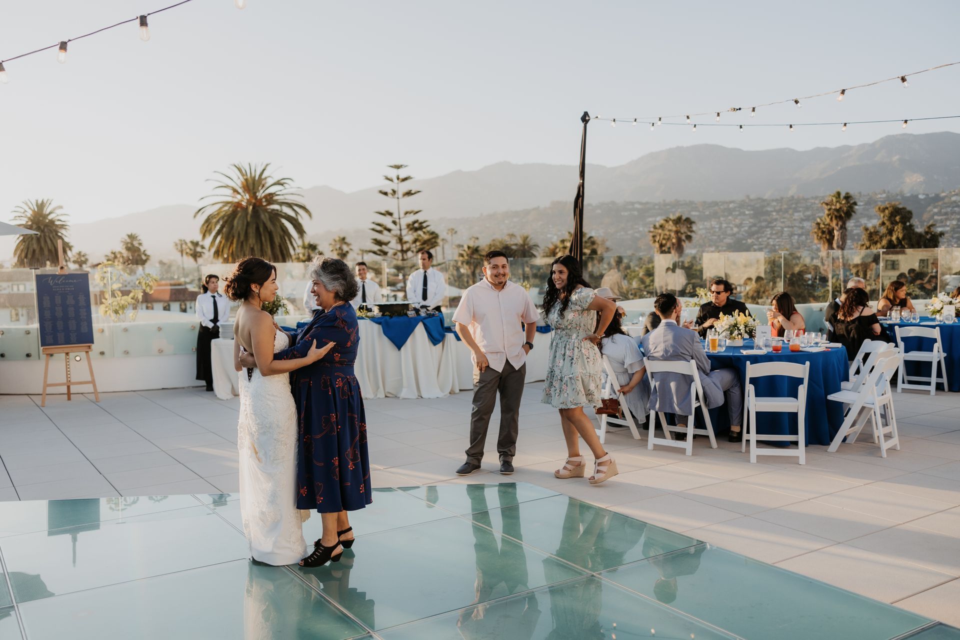 Guests mingle at an outdoor rooftop reception with tables, string lights, and mountain views.