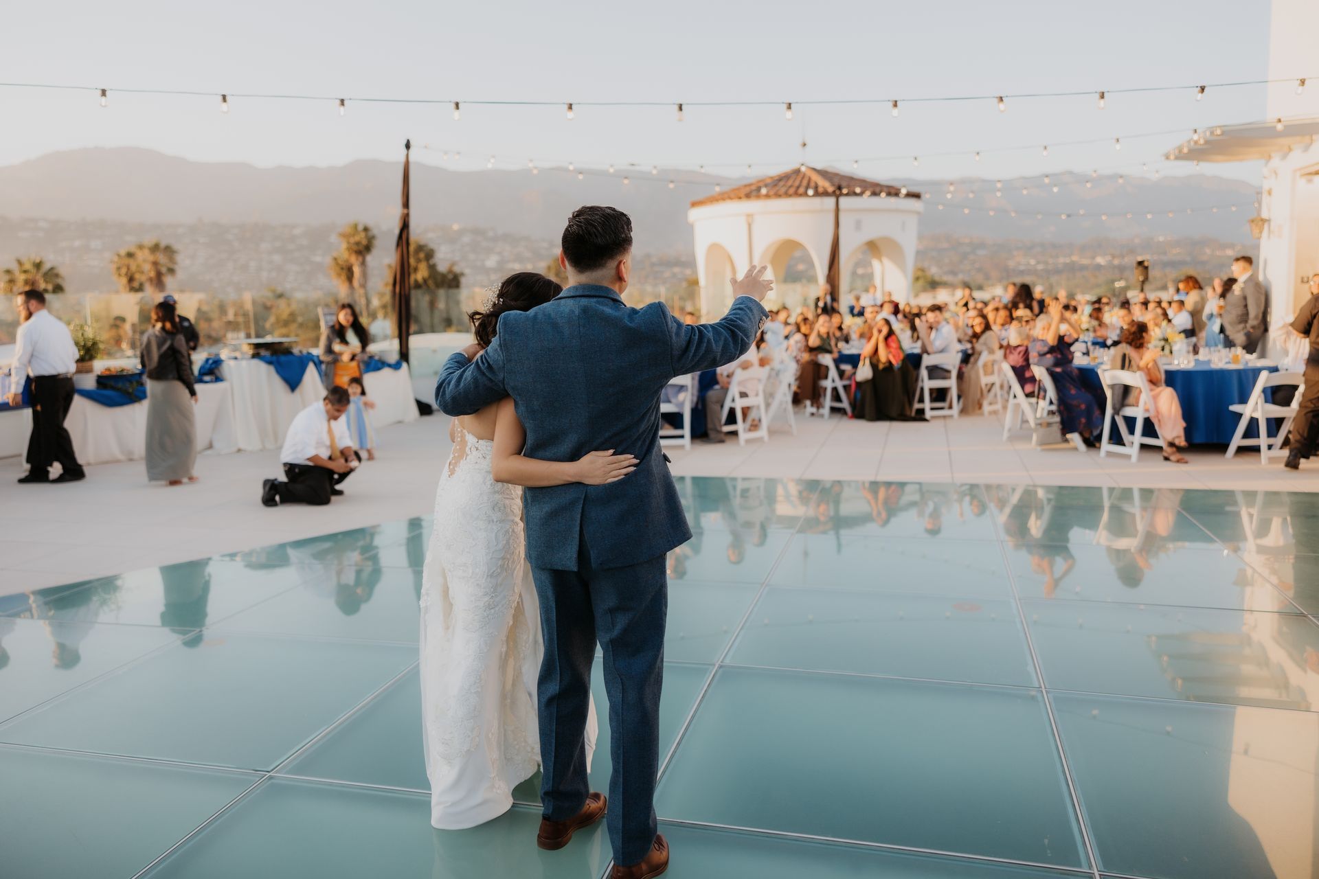 Couple embracing on a glass dance floor at an outdoor wedding reception under string lights