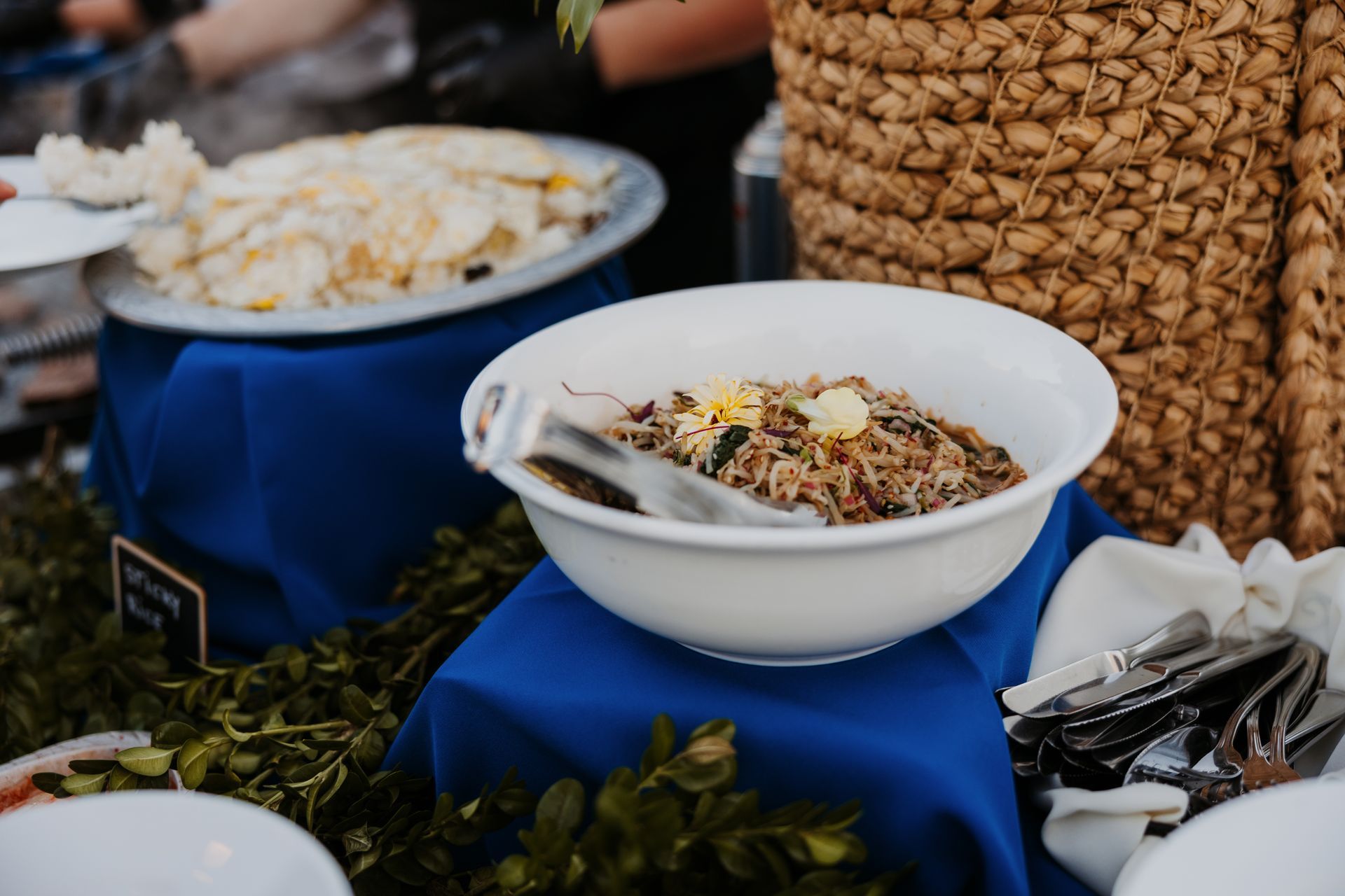 Buffet table with bowls of food, including rice and garnishes, set on blue cloth