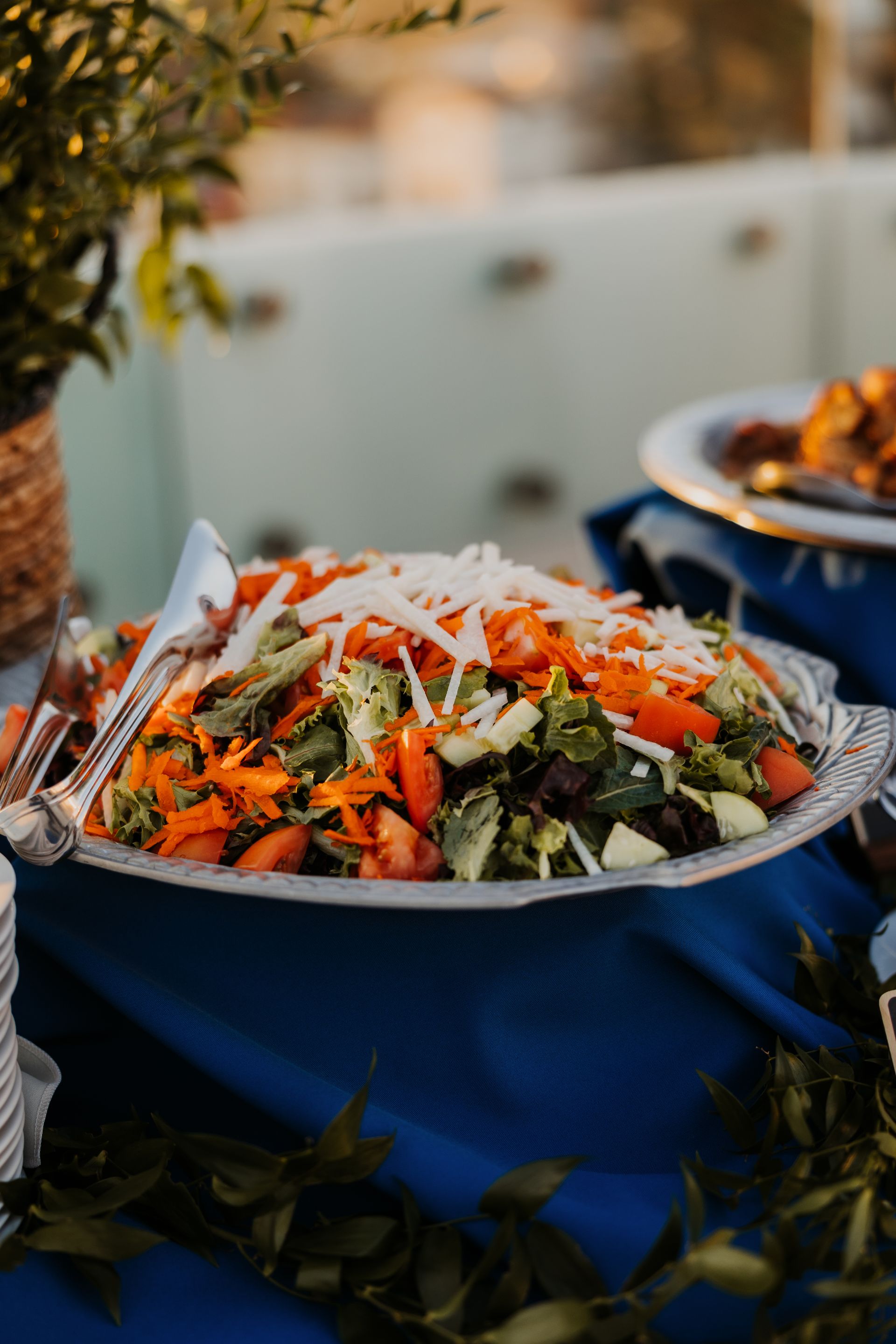 Large bowl of mixed salad with shredded carrots and greens on a blue cloth, outdoors at a table