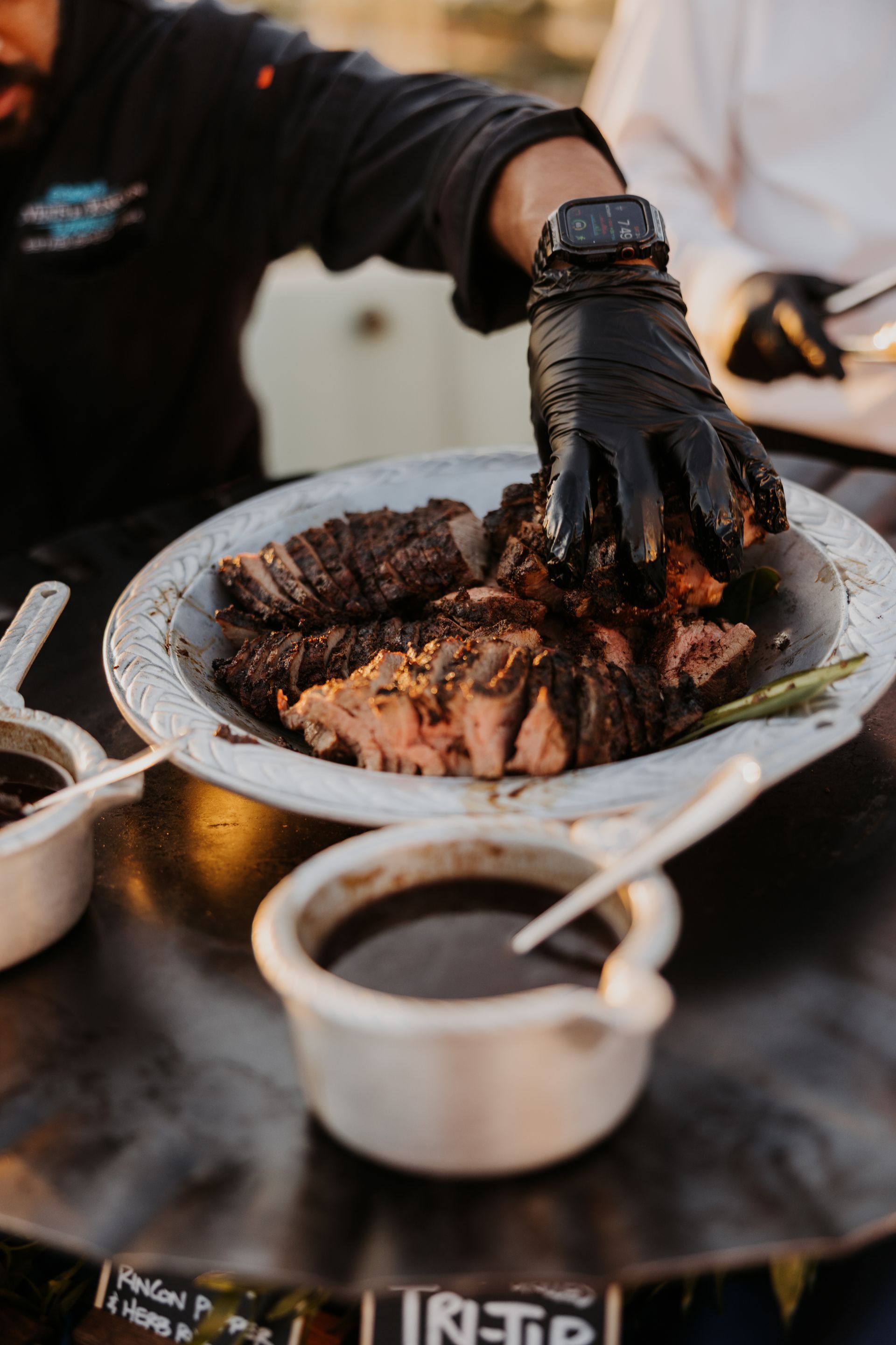 Gloved hands serving sliced grilled meat on a white plate at a dining table