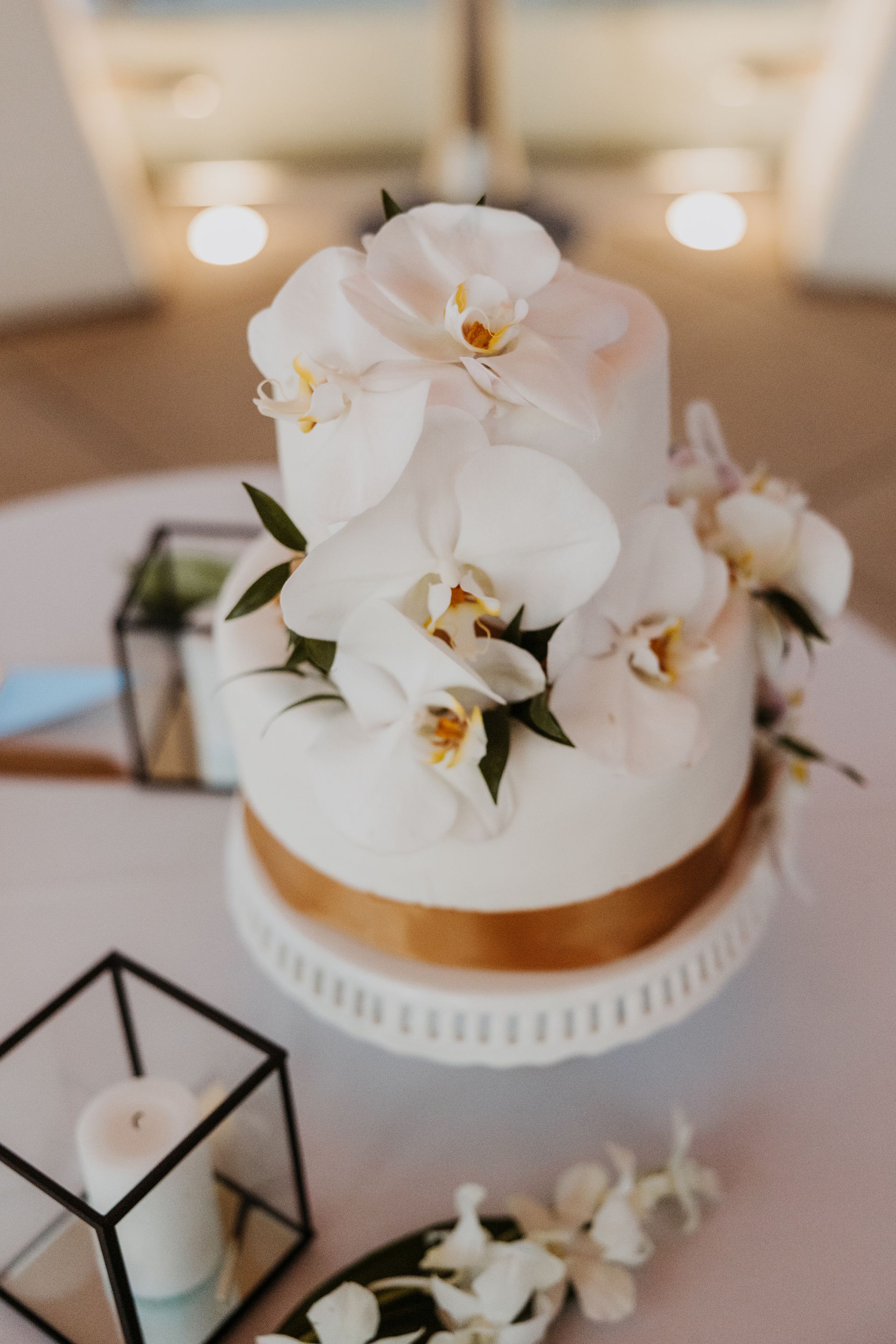 White floral wedding cake with orchids and gold ribbon on a decorated table