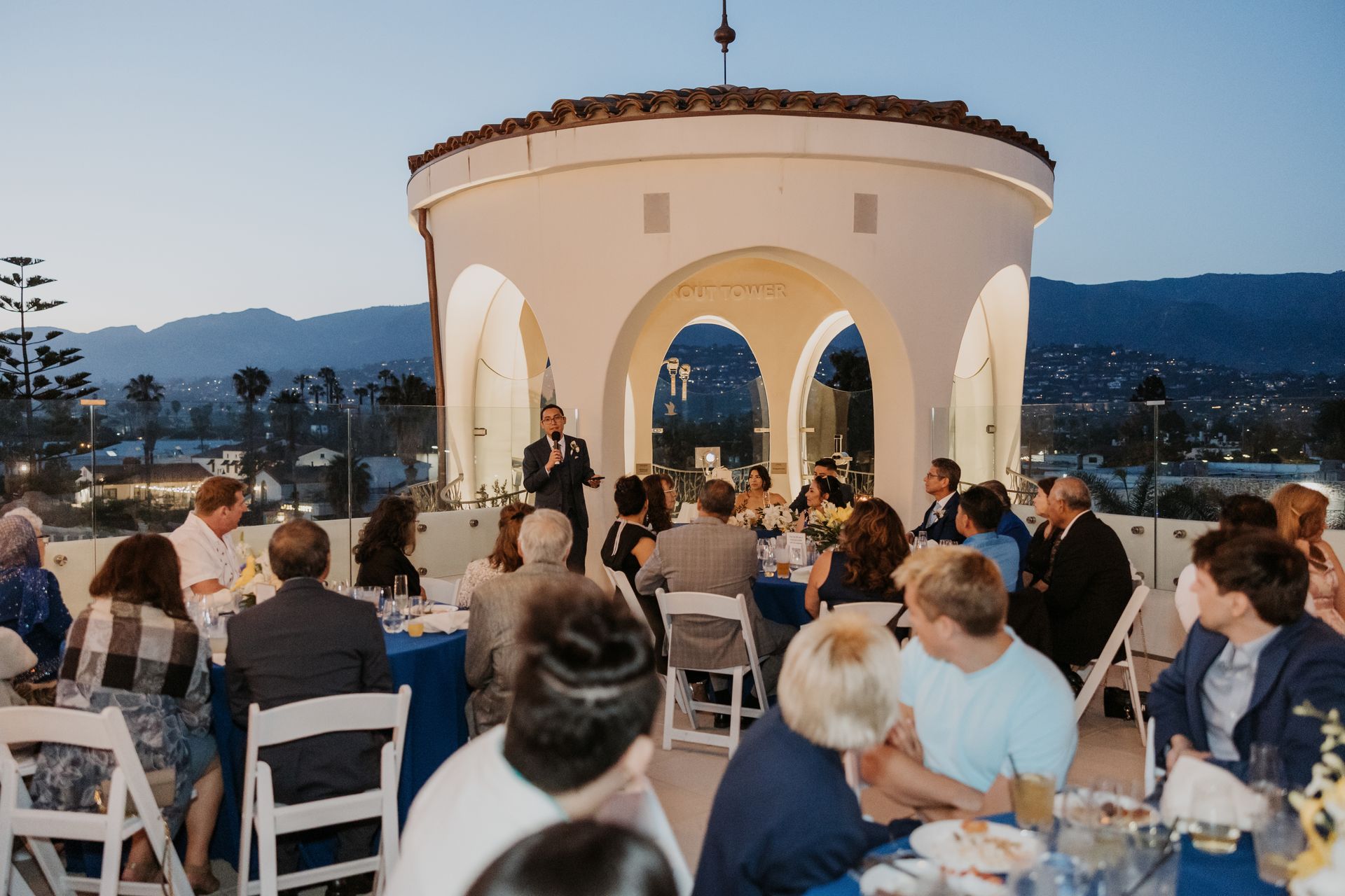 Outdoor wedding reception with guests seated around a white pavilion at sunset
