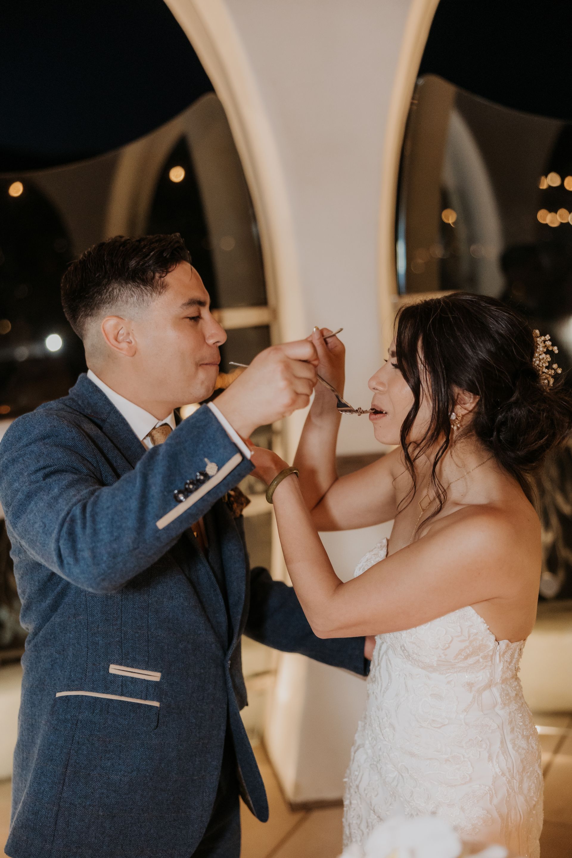 Two people in formal wear clink glasses at a wedding reception under warm evening lights.