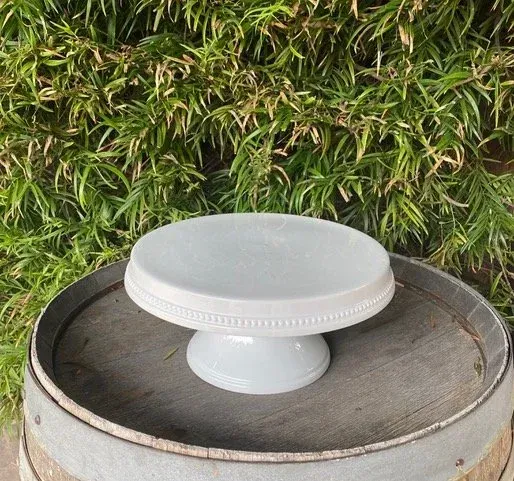 White cake stand on a metal surface with green foliage in the background