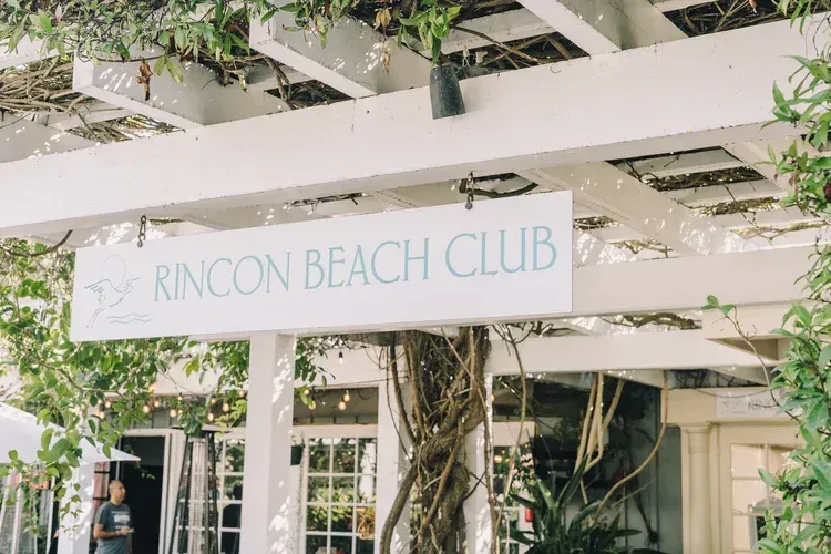 Sign reading “Rincon Beach Club” on a white pergola surrounded by greenery