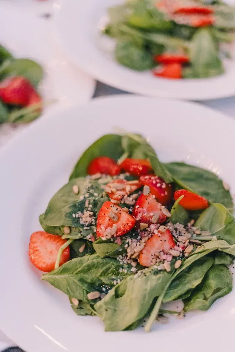 Strawberry spinach salad on a white plate with feta and sesame seeds