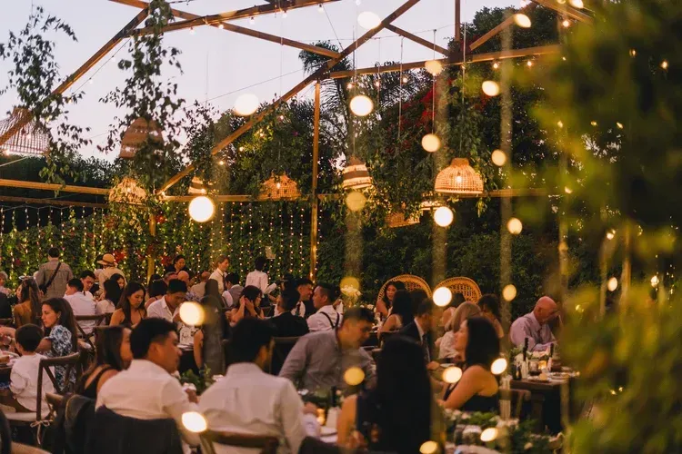 Guests dining under warm string lights at an outdoor evening party