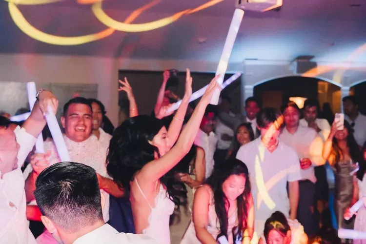 Crowded dance floor with people cheering under colorful lights at a party