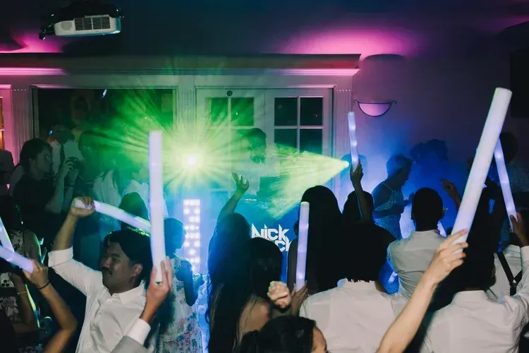 Crowd dancing at a neon-lit party with green and blue lights flashing in front of a house