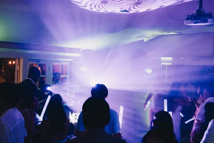 Crowd dancing in purple-blue nightclub lights with bright fog and laser beams