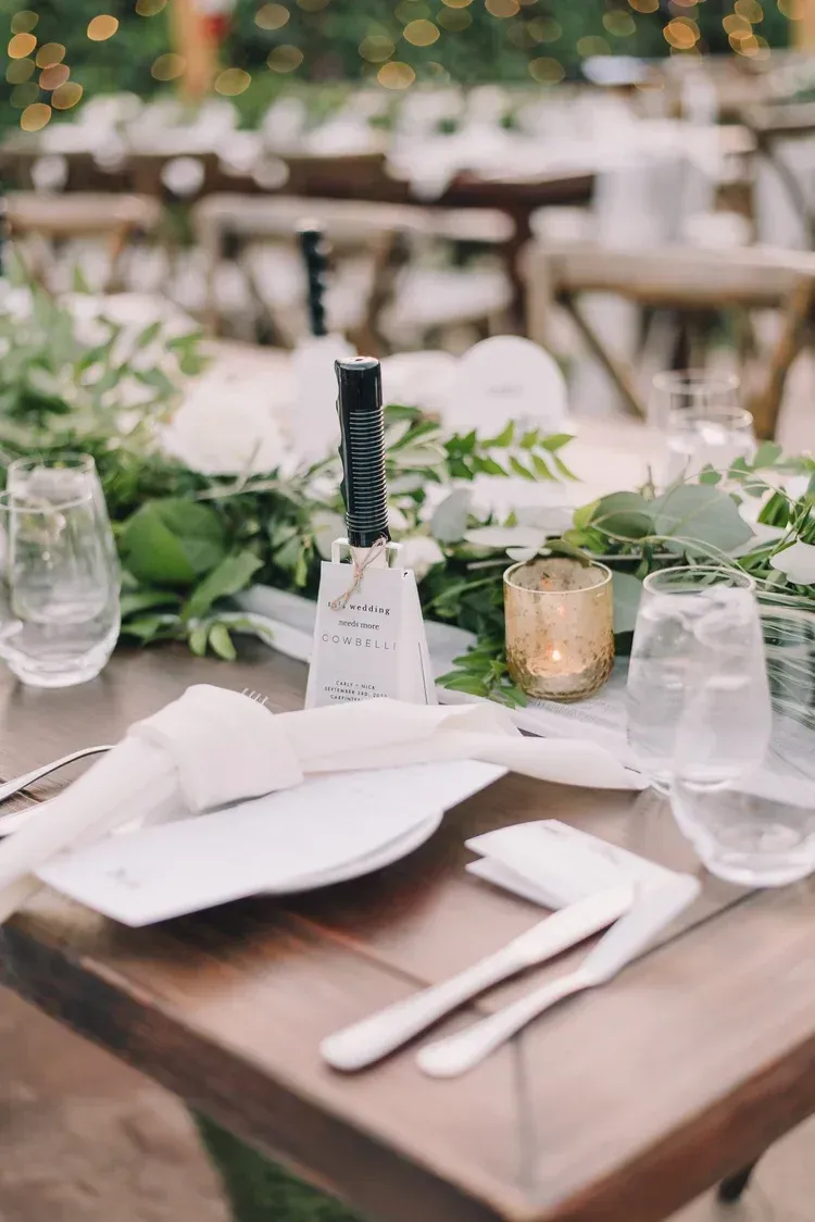 Set banquet table with white napkins, glassware, greenery, and candle centerpiece outdoors