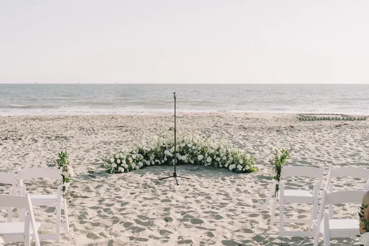 Beach wedding ceremony setup with white chairs and floral arch facing the ocean