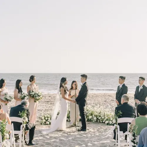 Bride and groom exchange vows at an outdoor beach wedding with floral decorations and seated guests