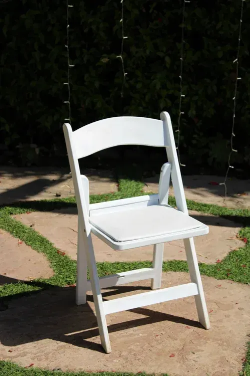 White folding chair on a sunlit stone path in a garden.