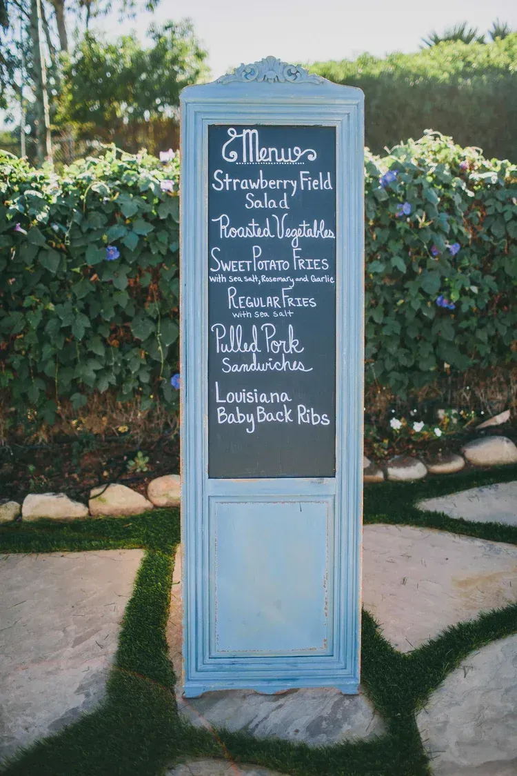 Blue signboard with chalk menu in a garden path beside hedges