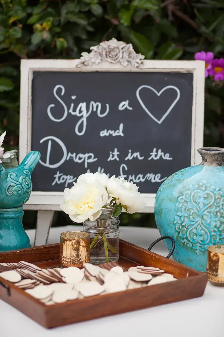 Sign-in chalkboard with hearts beside a decorative wedding guest book table and flowers