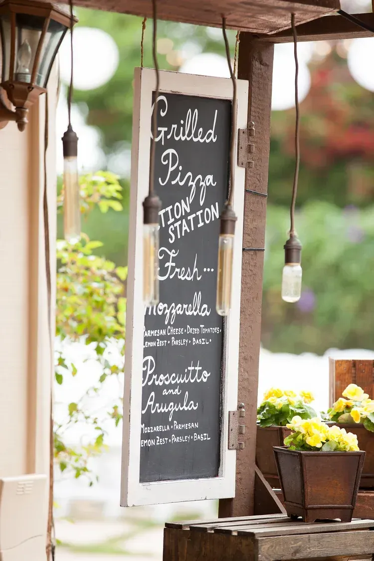 Chalkboard café menu sign hanging on a rustic patio with potted flowers and soft outdoor lights