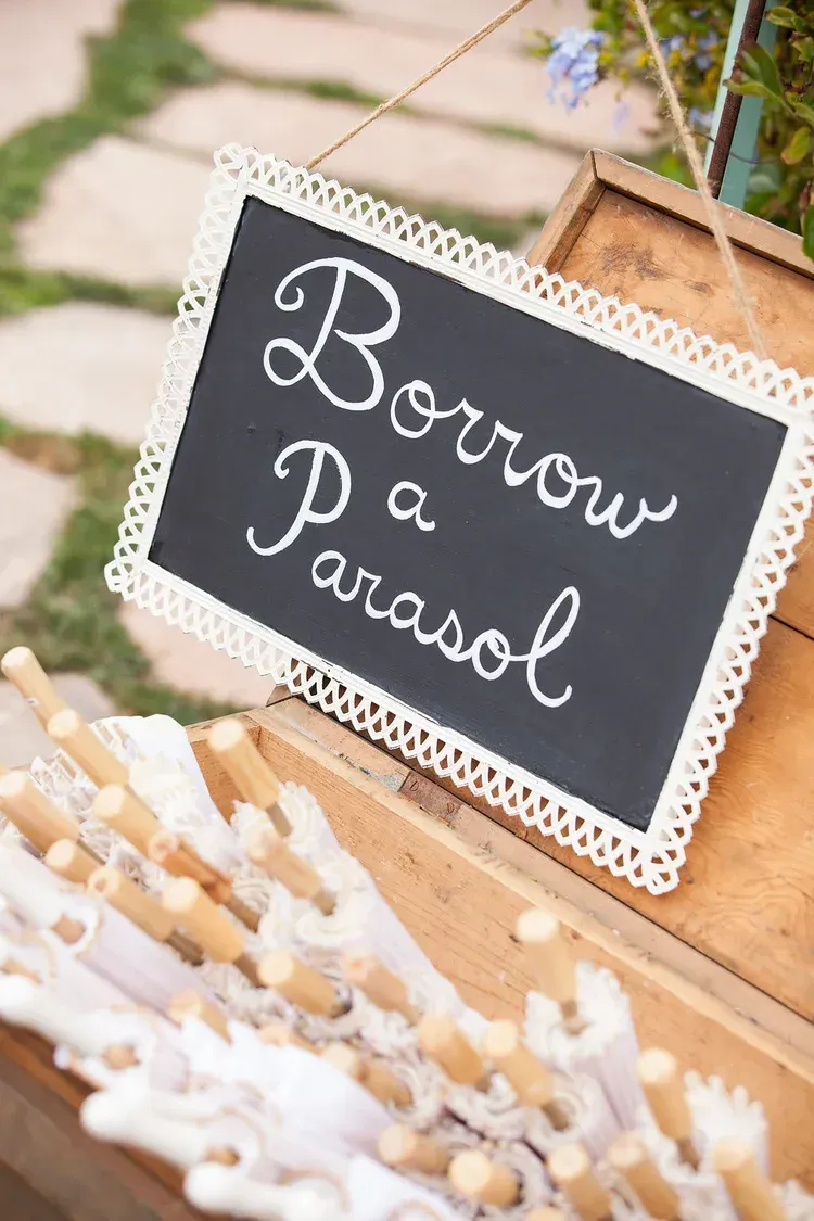 Black sign reading “Borrow a parasol” on a lace-decorated wooden crate outdoors