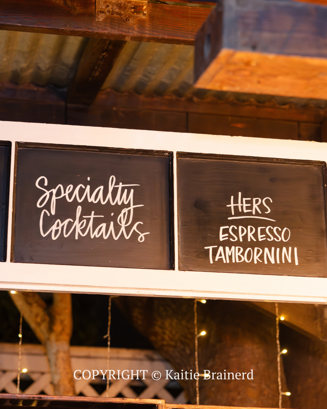 Specialty cocktails and “Hers espresso tamarind” signs on a dark menu board under a wooden roof.