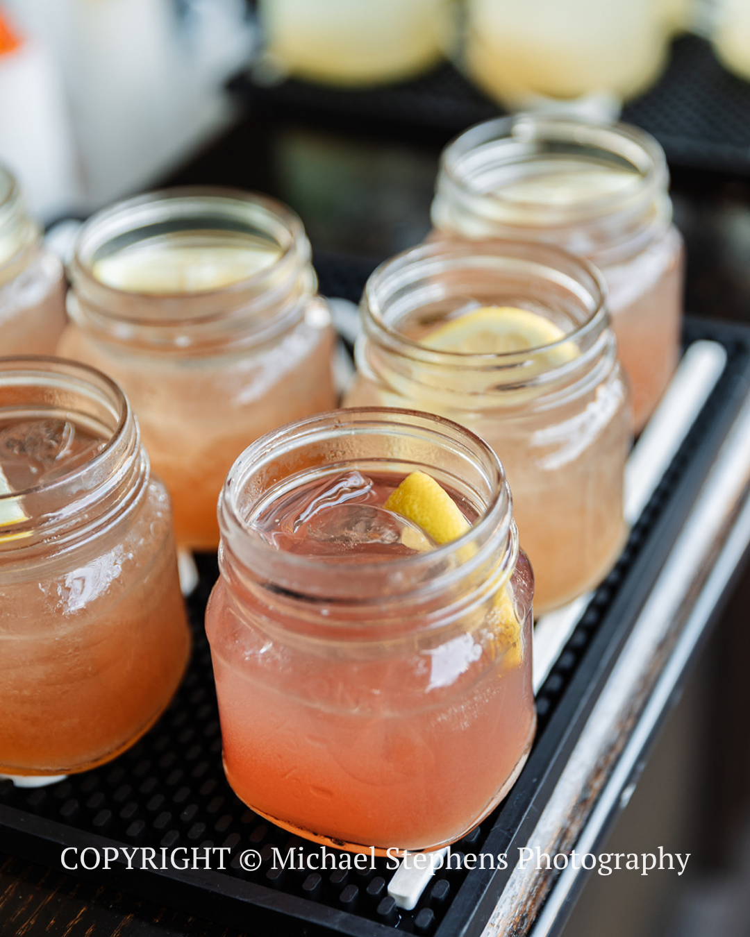 Mason jars of pink citrus drinks on a tray, one garnished with lemon slices.