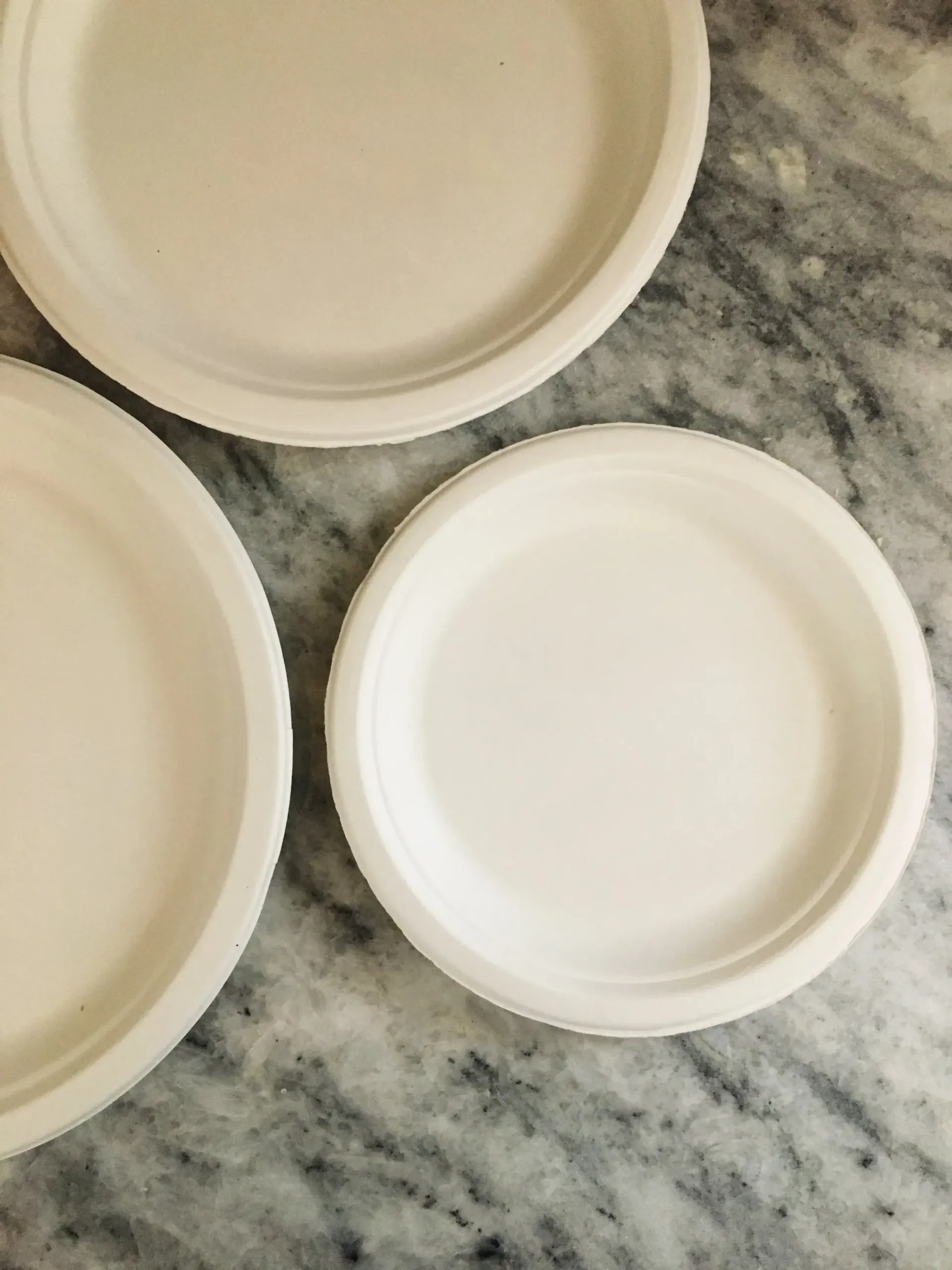 Three beige paper plates on a gray marble countertop.