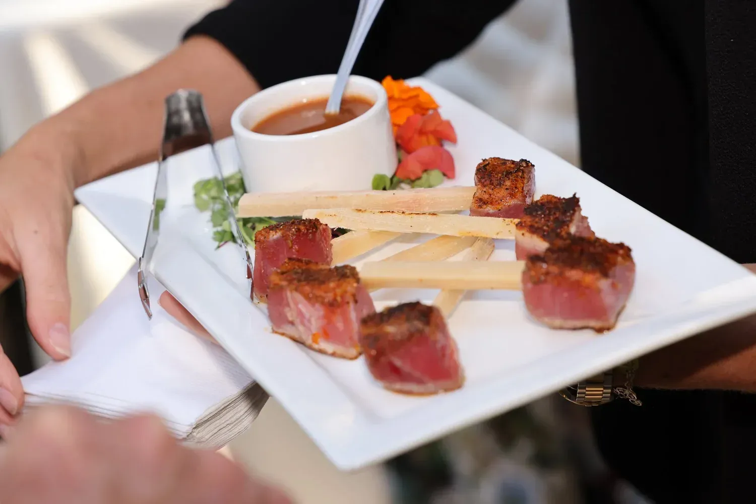 Gourmet meat skewers with sauce on a white plate, served with a small cup and spoon