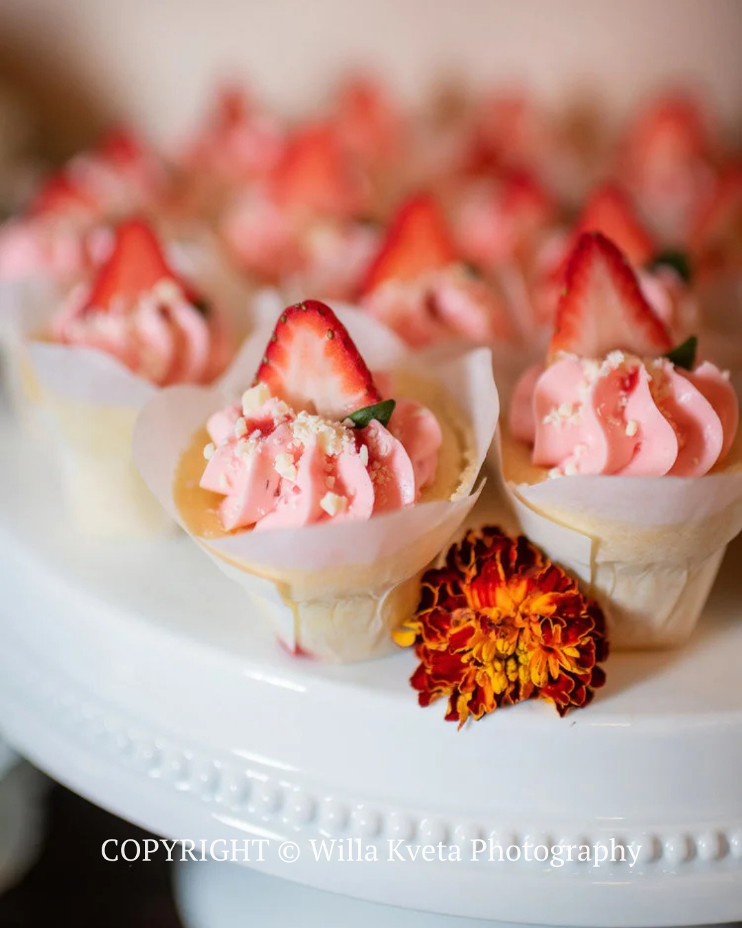 Strawberry cream dessert cups arranged on a white platter with a small orange flower garnish