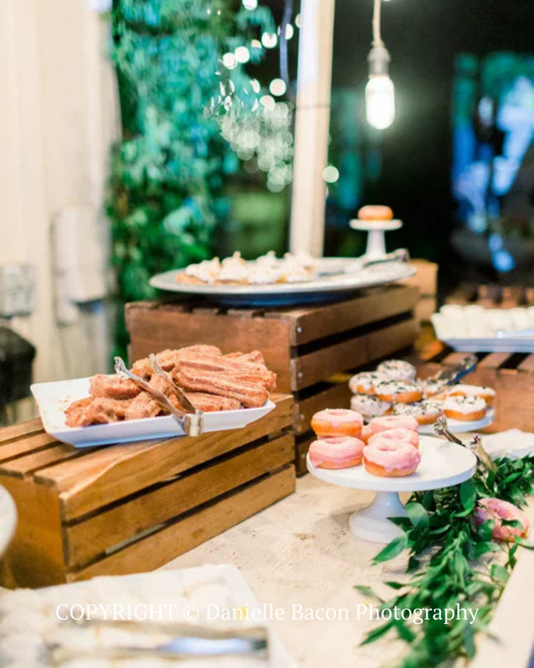 Dessert buffet with pastries and macarons on wooden crates at a softly lit indoor event table